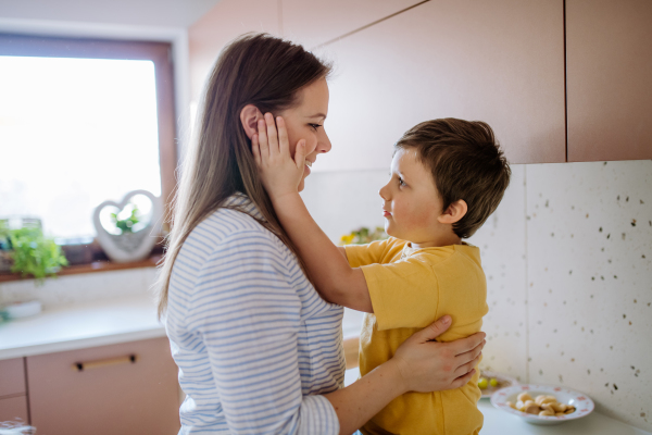 A happy young mother hugging her little son in kitchen at home.