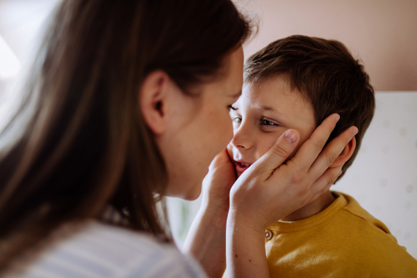 A happy young mother hugging her little son, caressing his cheeks, in kitchen at home.