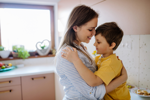 A happy young mother hugging her little son in kitchen at home.