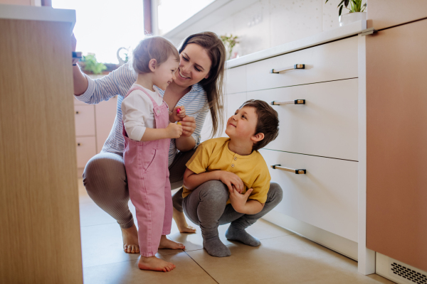 A young cheerful mother playing with her little children and having fun in kitchen.