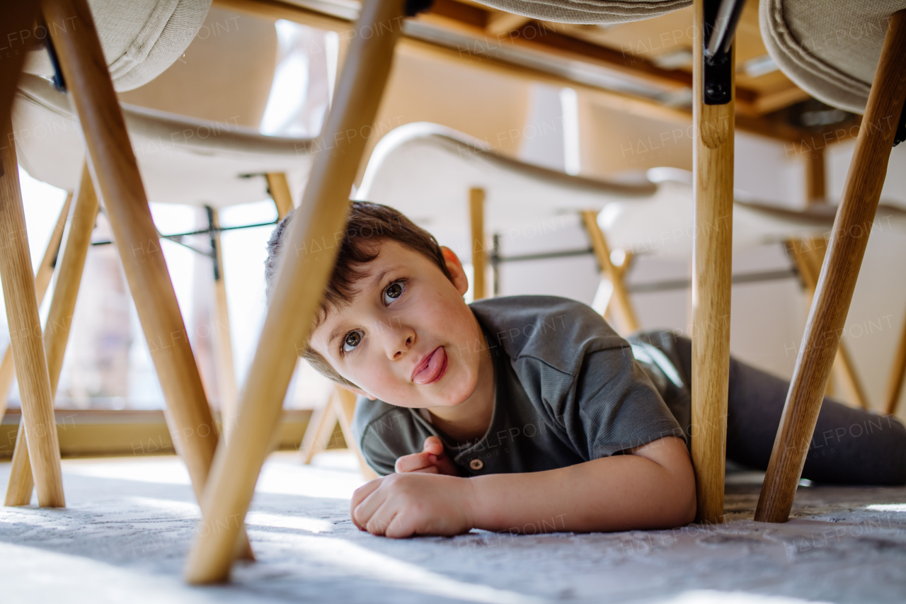 A lttle boy hiding under the chair at home and making grimace.