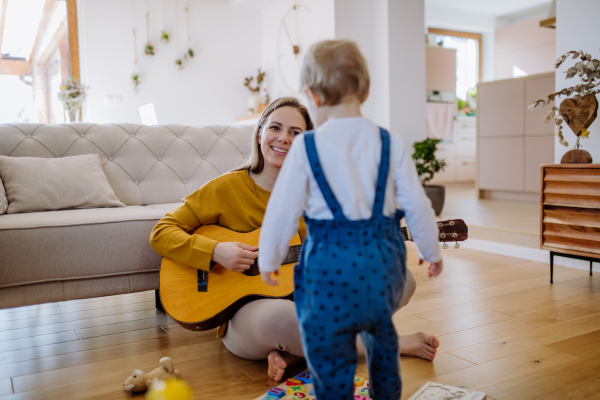 A happy family. Mother and daughter playing guitar at home. Adult woman playing guitar for child girl