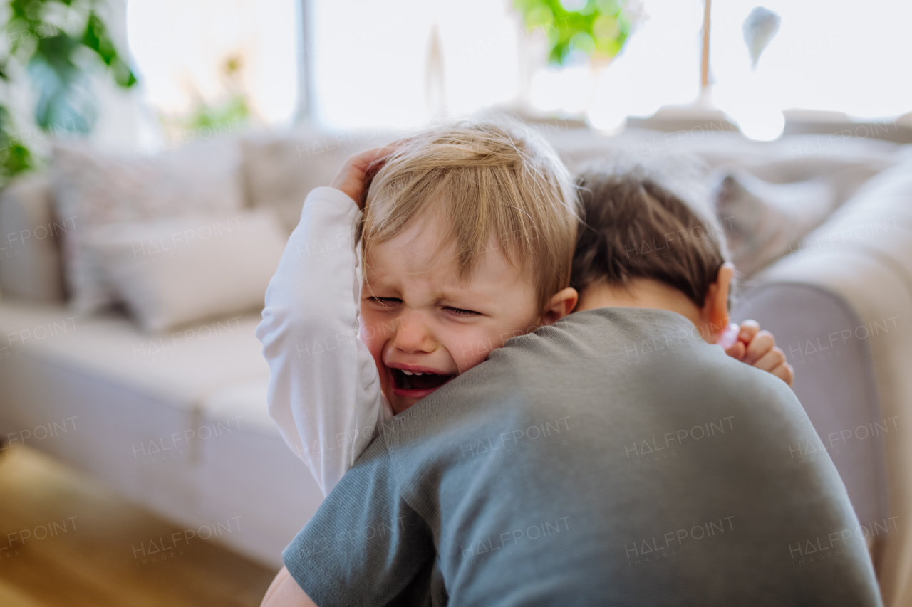 Little brother hugging his crying sister, consoling her in their living room.