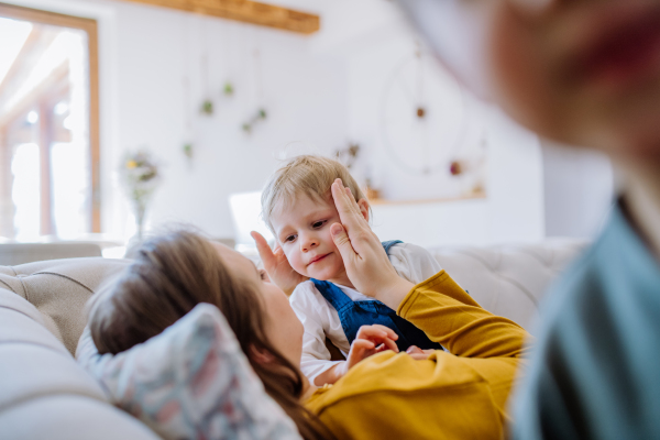 A young cheerful mother playing with her little children and having fun in their living room.