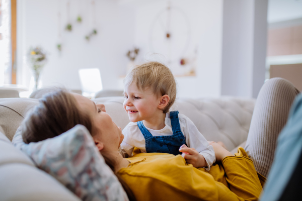 A young cheerful mother playing with her little child and having fun on sofa.