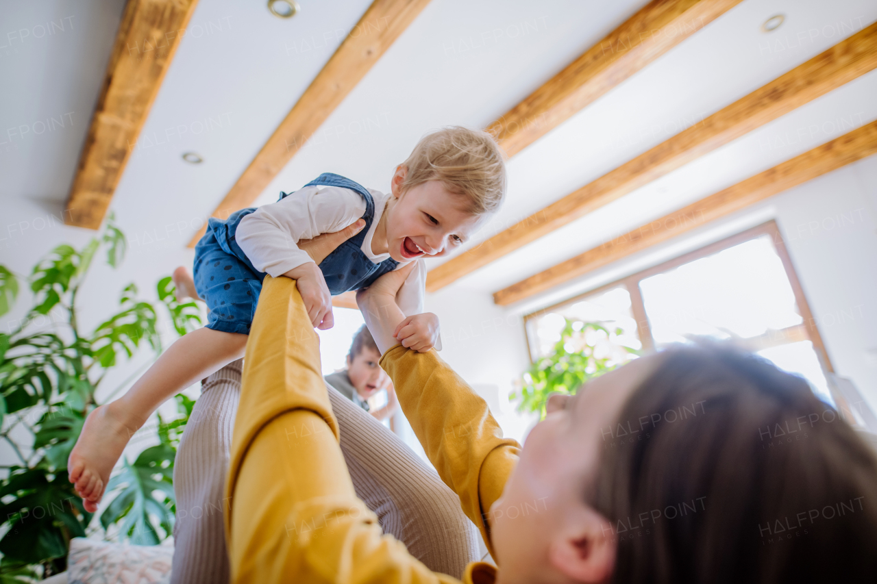 A young cheerful mother playing with her little children and having fun when lifting them up on sofa.