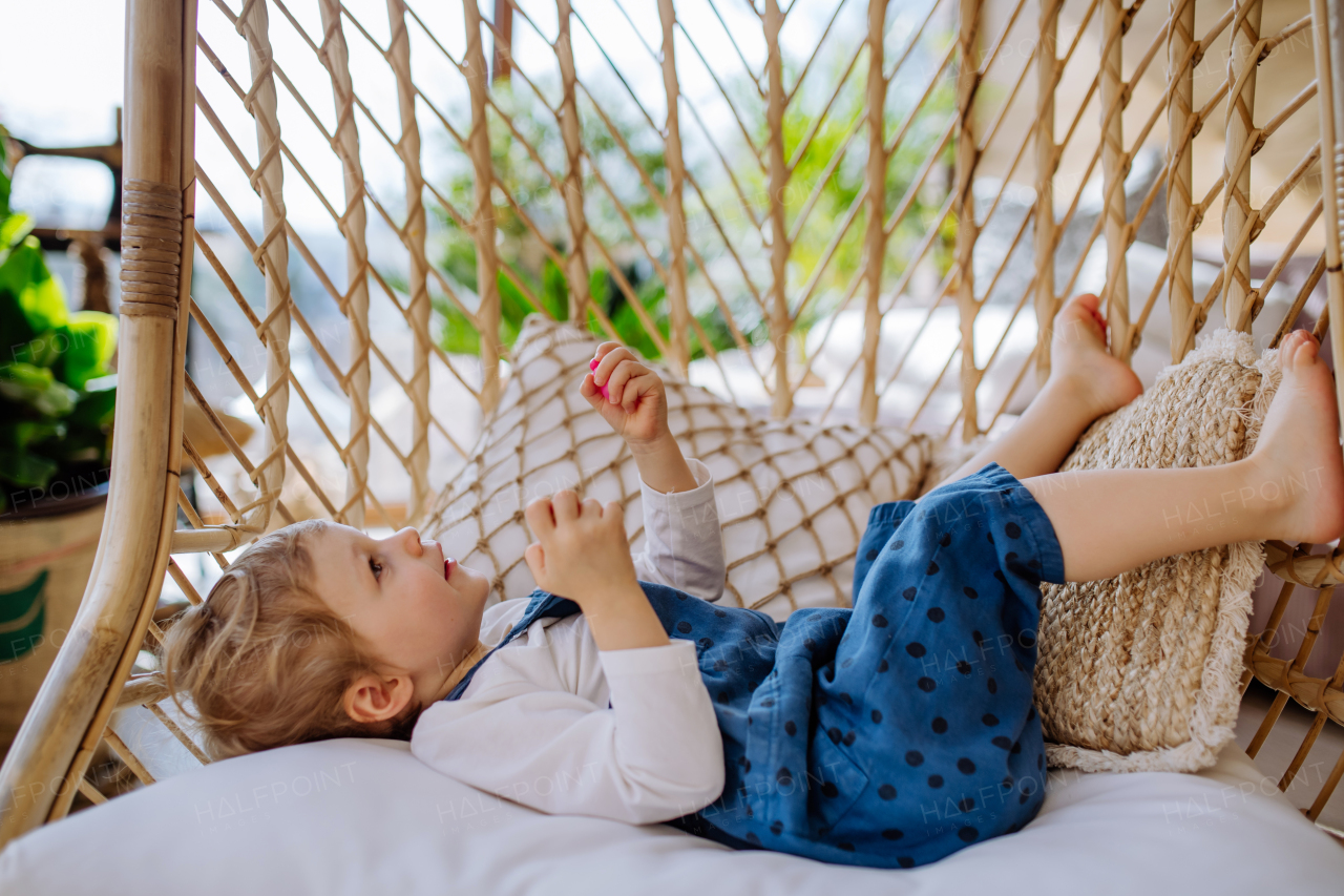 Little girl lying playing, and swinging on a hanging chair in conservatory at home.