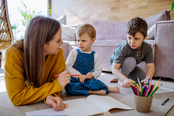 A happy mother with her little children at home drawing together.