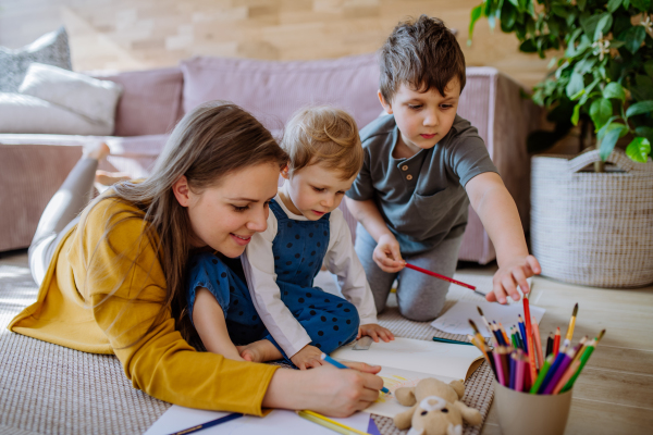 A happy mother with her little children at home drawing together.