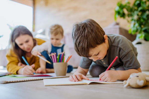 A happy mother with her little children at home drawing together.