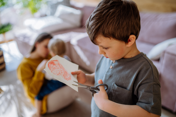 A little boy cutting drawn picture, having creative time in home.