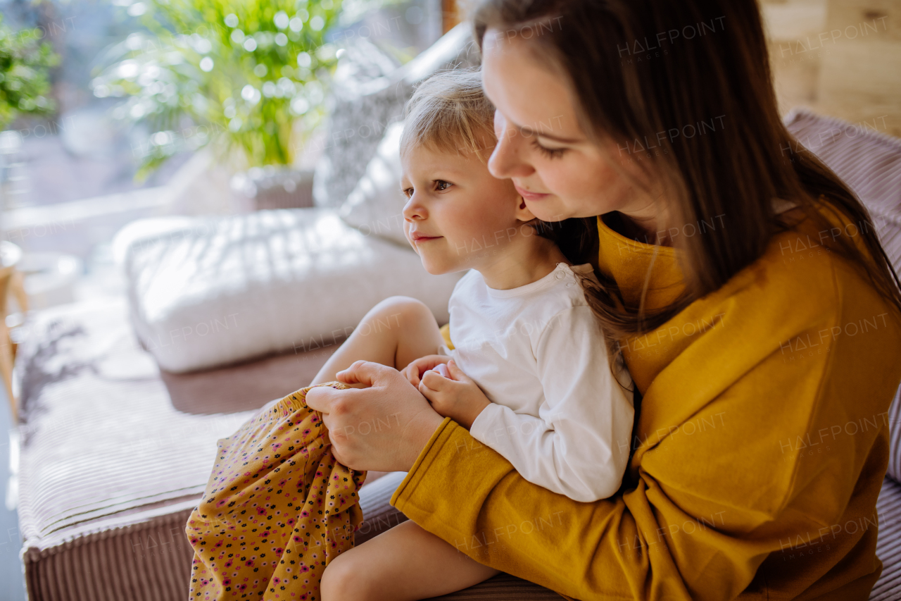 Young mother dressing up her little cute daughter in their home, moterhood concept.