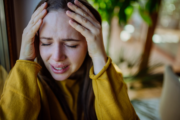 A woman suffering from depression and crying at home, holding head in her hands.