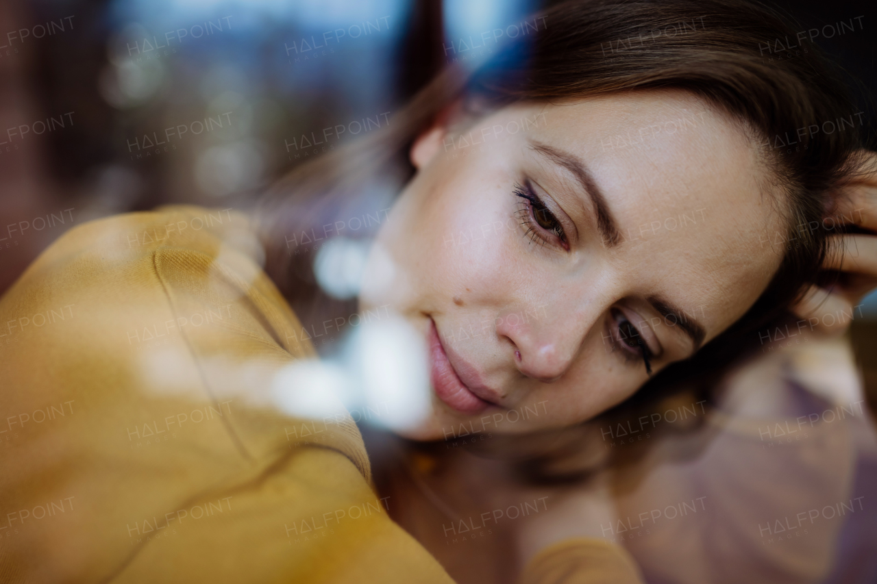 A close-up portrait of happy young woman resting at home, shot through window.