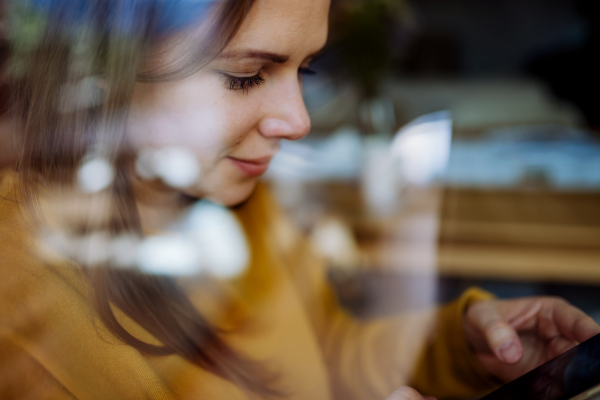 A close-up portrait of happy young woman resting at home, shot through window.