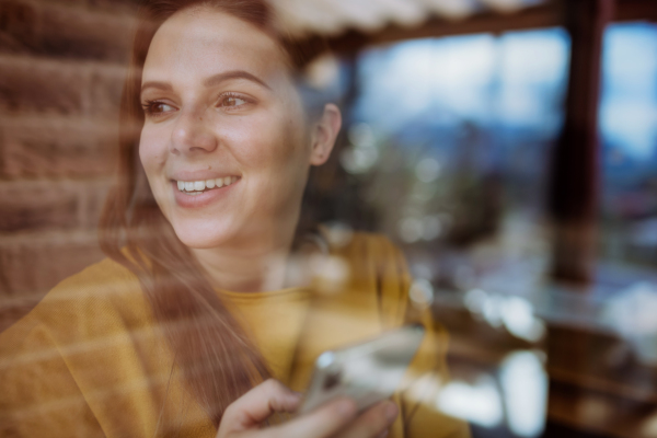 A close-up portrait of happy young woman resting at home, shot through window.