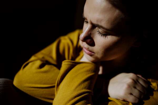 A woman suffering from depression and lying on floor with her hands covering head on black background.