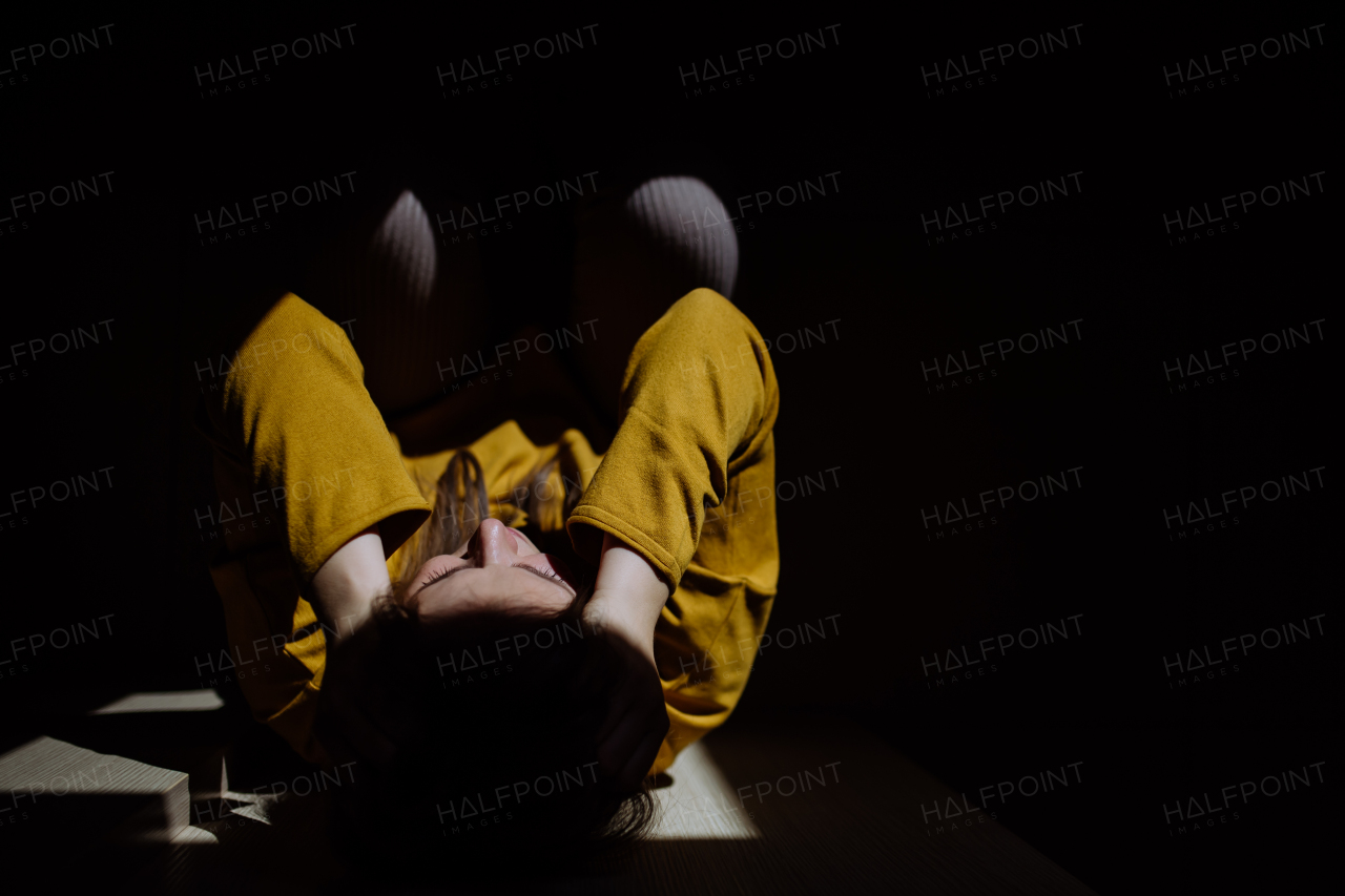 A woman suffering from depression and lying on floor with her hands covering head on black background.