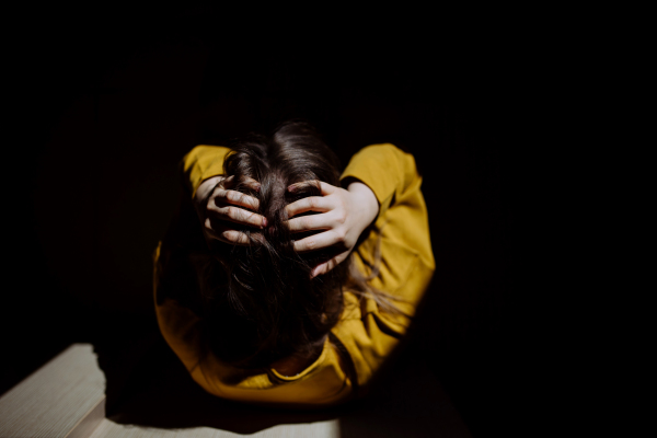 Top view of unrecognisable woman suffering from depression and crying at home, holding head in hands.