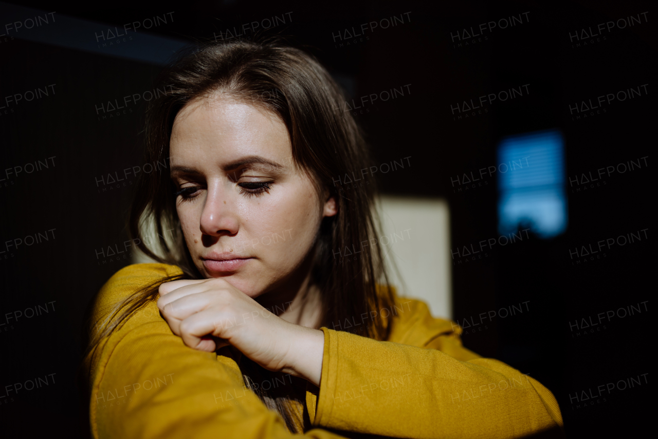 Young woman suffering from depression at home, crying and looking trough the window.