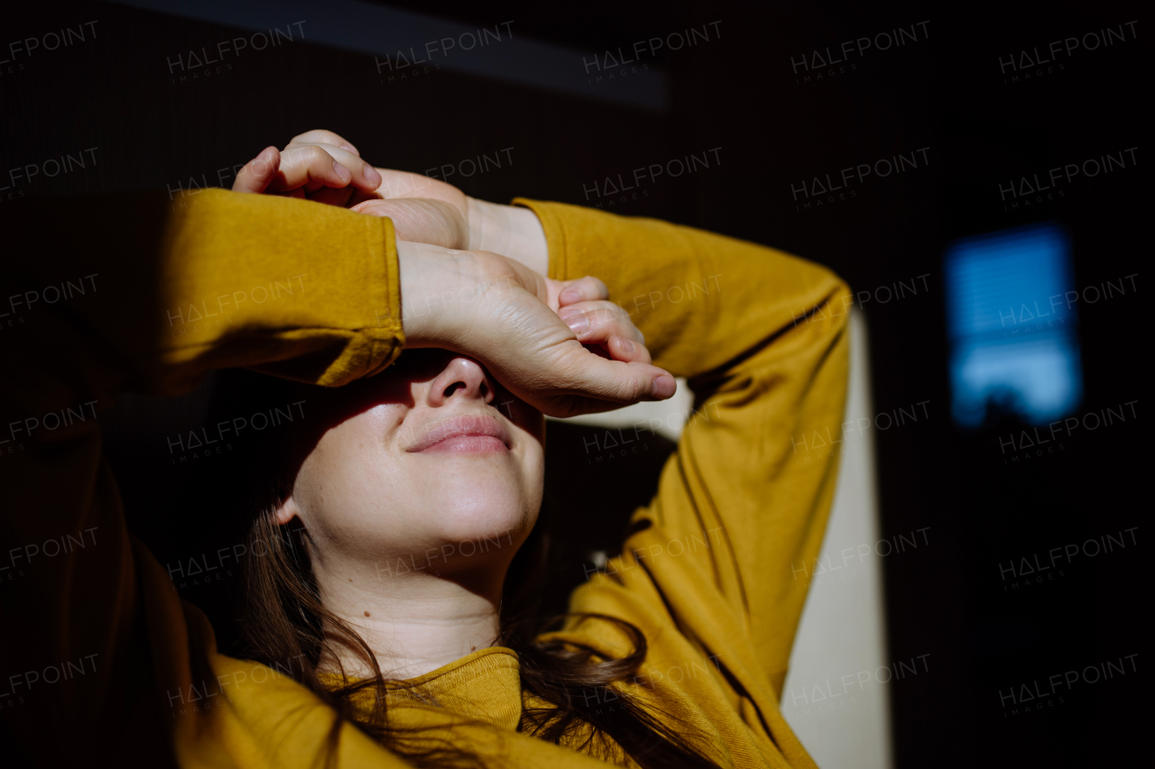 A woman suffering from depression and lying on floor with her hands covering head on black background.