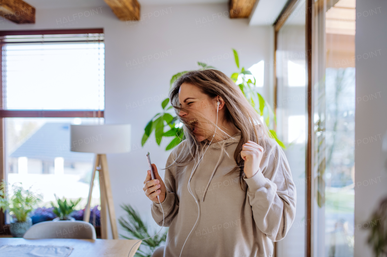 A happy young woman with earphones dancing, enjoying leisure weekend at home, stress free concept