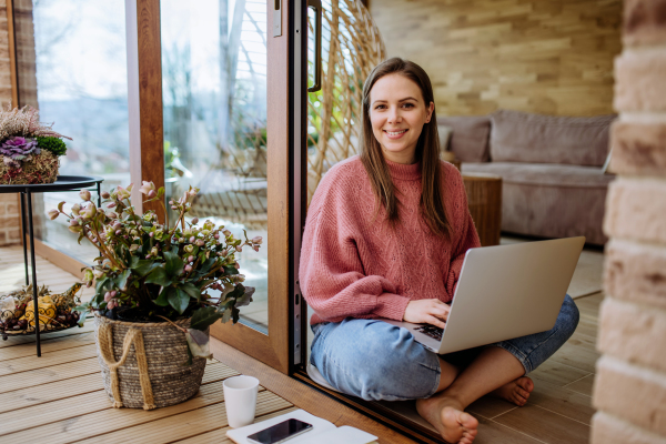 A young college student studying on laptop, when sitting on floor at home.