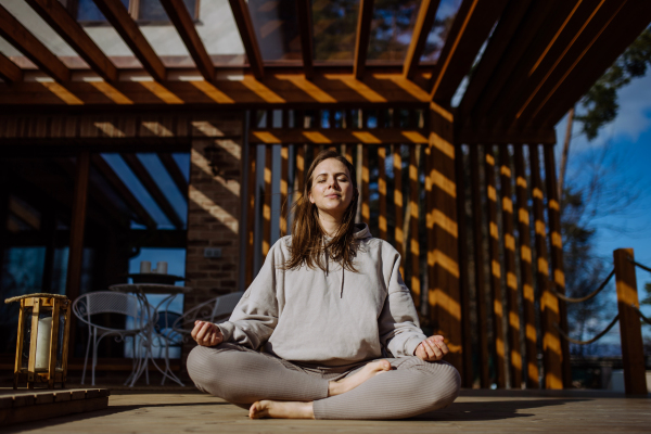 A young woman doing breathing exercise outside on terrace at home.