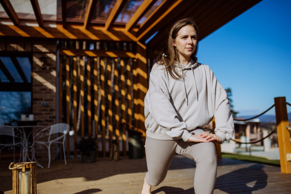 A young woman exercising, doing yoga and stretching outside on terrace at home.