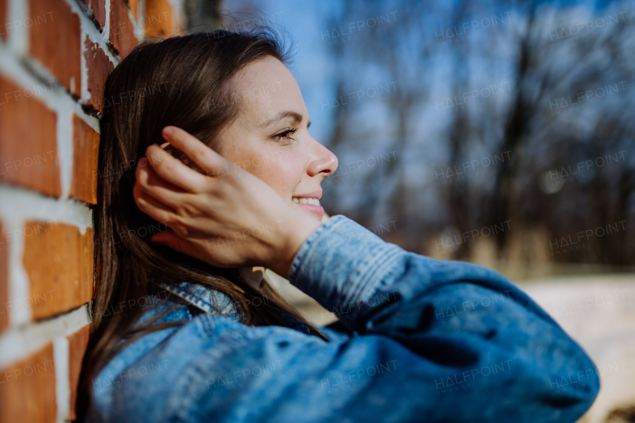 A side view portrait of young woman in denim jacket leaning the brick wall outdoors in summer