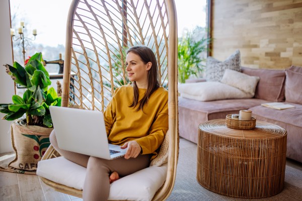 Work from home or study online, concept with a woman working at laptop outdoor on terrace, sitting in hanging chair.