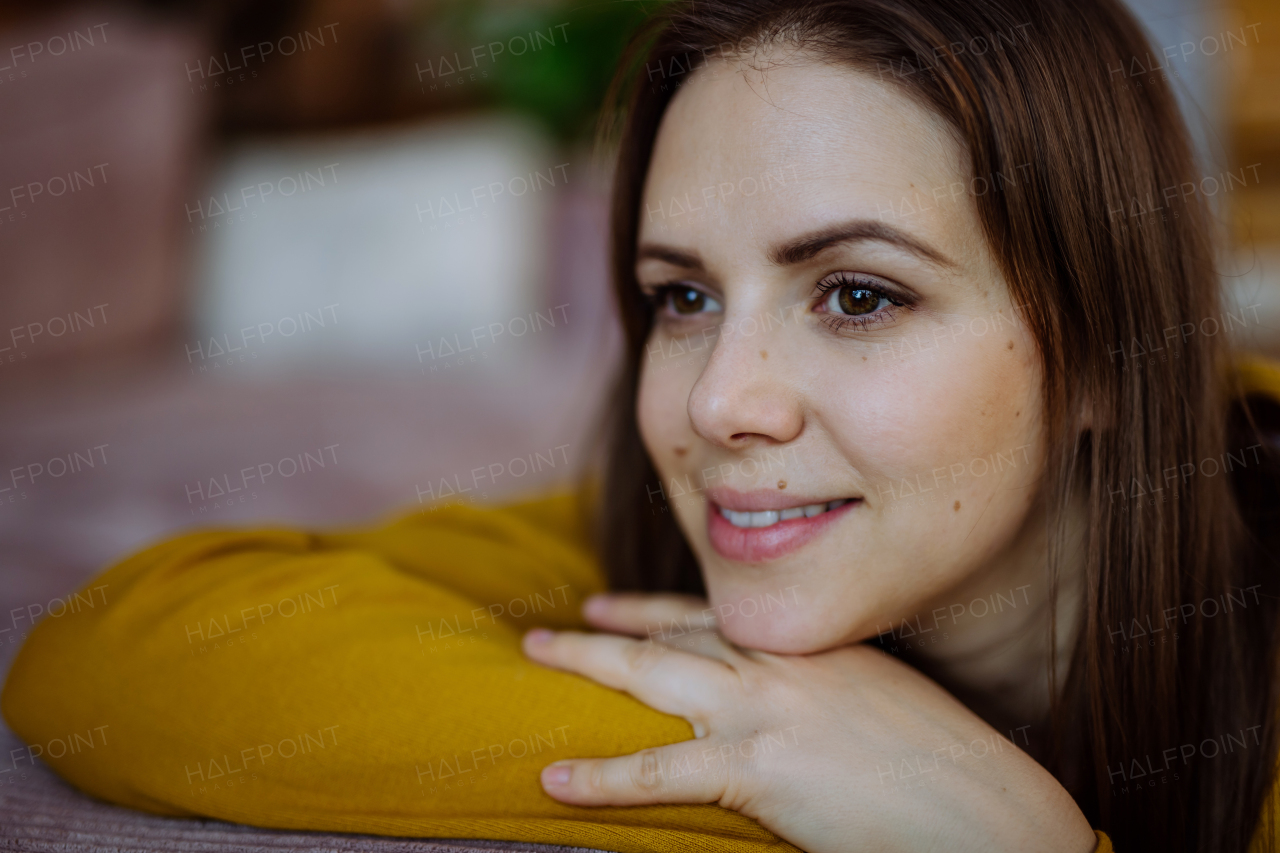 A close-up portrait of happy young woman smiling and looking at camera when restin on sofa at home.