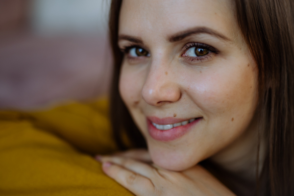 A close-up portrait of happy young woman smiling and looking at camera when restin on sofa at home.