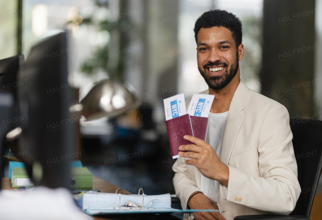 Young happy man holding plane tickets in an office.