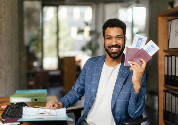 Young happy man holding plane tickets in an office.