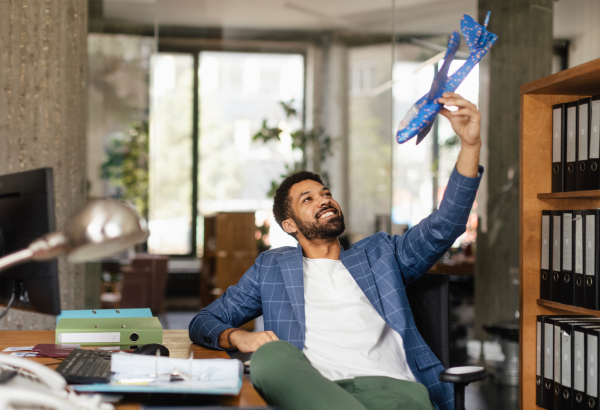 Young happy man holding model of plane in an office. Male travel agent working in travel agency.