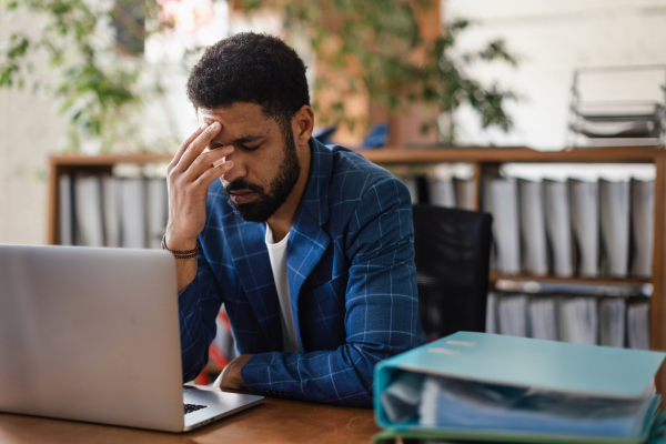 Young exhausted male employee in front of notebook in his office. Signs of burnout at work.