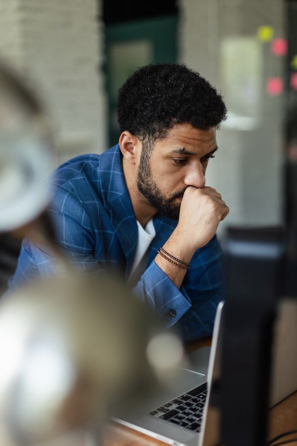 Young tired man sitting in front of laptop in his office.