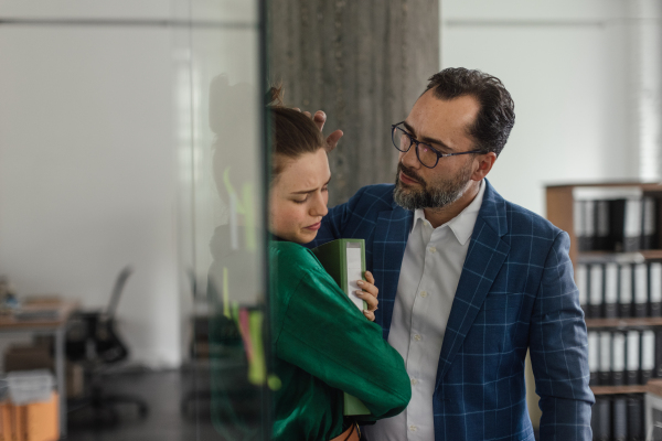 Mature man abusing his younger colleague, concept of harassment at work. Young female feeling under pressure, lacking personal space.