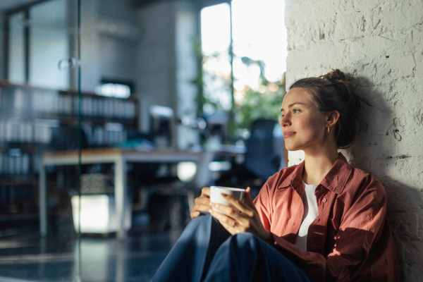 Happy female entrepreneur in her own office drinking coffee. Moment of peace after workday. Woman-owned business.