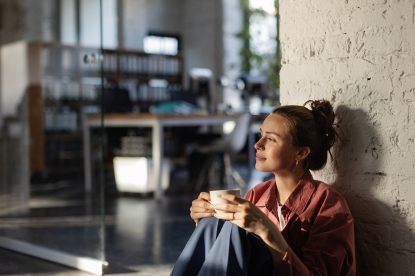 Happy female entrepreneur in her own office drinking coffee and watching sunset. Moment of peace after workday. Woman-owned business.