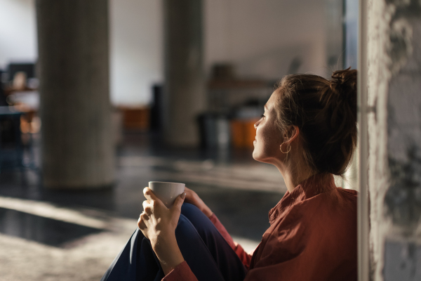 Happy female entrepreneur in her own office drinking coffee and watching sunset. Moment of peace after workday. Woman-owned business.