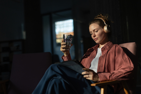 Young woman stting in armchair, listening music and working on a digital tablet.