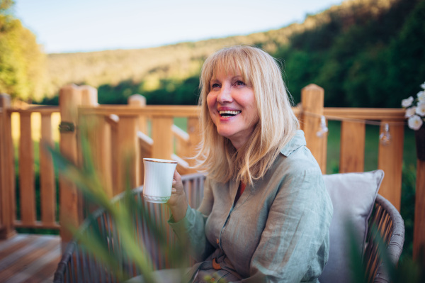 A happy mature woman relaxing with morning coffee on terrace in summer.