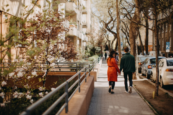 A rear view of young couple in love walking outdoors at the city street, holding hands