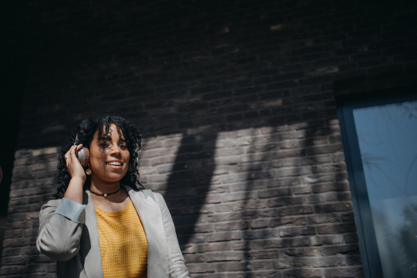 A young biracial woman wearing headphones and enjoying listening to music outdoors in street.