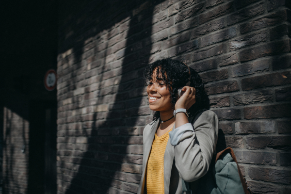 A young biracial woman wearing headphones and enjoying listening to music outdoors in street.