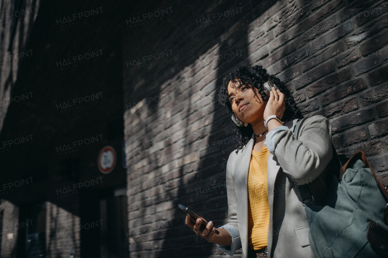 A young biracial woman wearing headphones and enjoying listening to music outdoors in street.