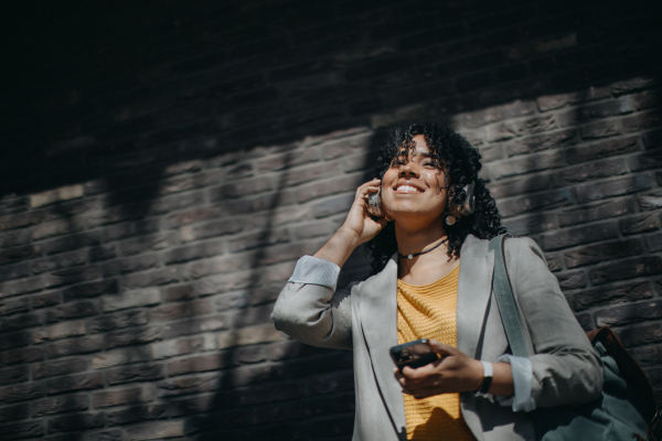 A young biracial woman wearing headphones and enjoying listening to music outdoors in street.