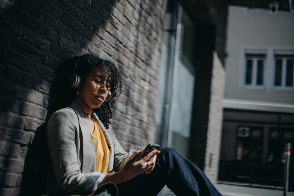 A young biracial woman wearing headphones and enjoying listening to music outdoors in street.